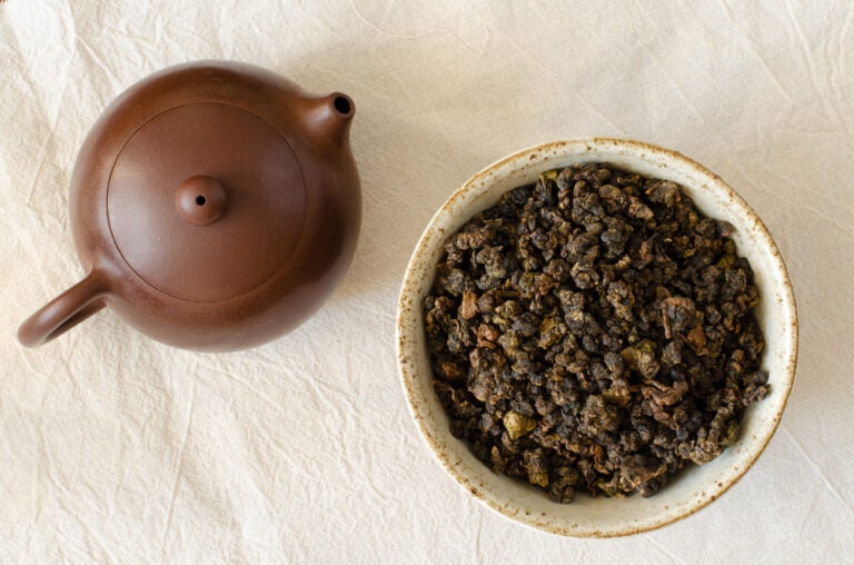 台湾お土産として定番の台湾茶。白い布の上に置かれた茶褐色の急須と、素朴な器にたっぷりと盛られた丸まった烏龍茶の茶葉が並んでいる様子