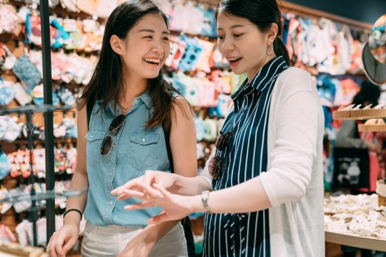 予算に合わせた台湾のお土産選び。色鮮やかな雑貨が並ぶ土産物店で、二人の女性が笑顔で商品を眺めながらショッピングを楽しんでいる様子
