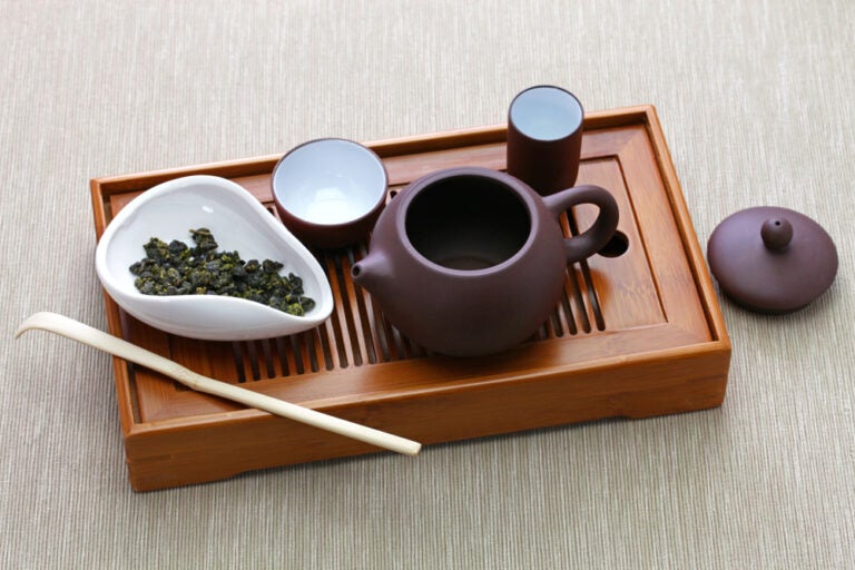 台湾お土産として人気の台湾茶器。木製の茶盤の上に紫褐色の急須や湯呑みが並び、白い器には丸まった烏龍茶の茶葉が用意された本格的なティーセットの様子