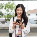 駅のホームでスマートフォンを操作している旅行者の女性