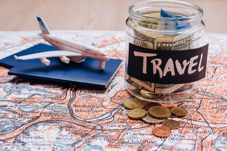 地図の上に置かれた「TRAVEL」と書かれた貯金瓶と硬貨、模型飛行機が並ぶ旅行費用のイメージ