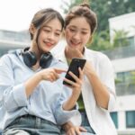 旅行中の2人の女性が、スマートフォンで通信サービスを利用しながら情報を確認している様子