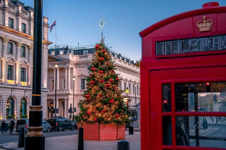 イギリス名物の赤い電話ボックスの横にライトアップされたツリーが飾られた、ホリデーシーズンの華やかなロンドンの街並み
