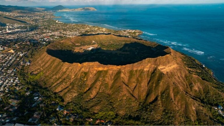 ハワイ・オアフ島にあるダイヤモンドヘッドの火山クレーターと、周囲に広がる海岸線と街並みの空撮風景