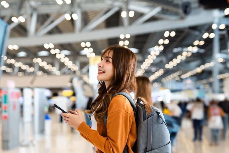 空港でスマートフォンを手にする旅行者。eSIM対応機種を確認して海外旅行へ出発する様子