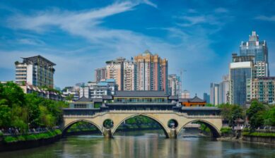晴天のもと、錦江にかかる安順廊橋と高層ビル群が並ぶ成都中心部の風景を紹介する写真