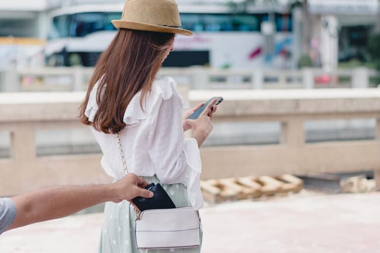 スマートフォンを操作中の女性旅行者のバッグから財布を盗もうとするスリの手。