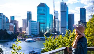 展望スポットからブリスベン川と高層ビル群を眺める帽子をかぶった女性旅行者