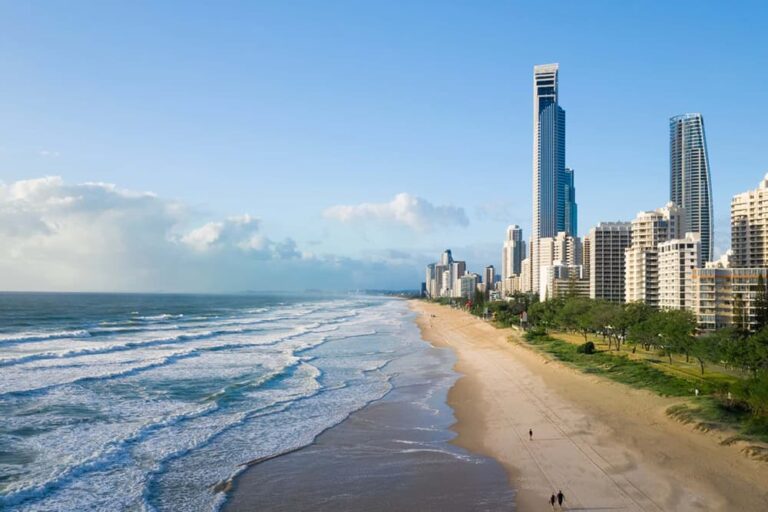 白い波が打ち寄せるゴールドコーストの長い砂浜と、海岸沿いにそびえる高層ビル群を空から捉えた風景