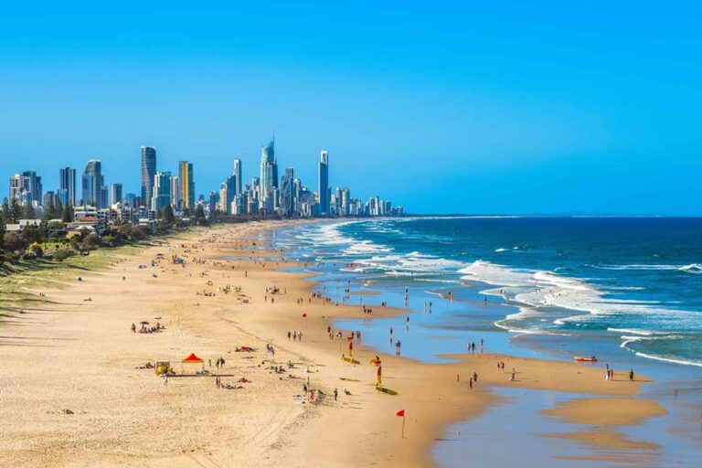 快晴のゴールドコーストで海水浴客やライフセーバーの旗が点在する広大なビーチの全景