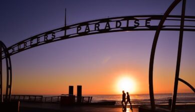サーファーズパラダイスのゲートアーチ越しに見える夕日とシルエットの観光客