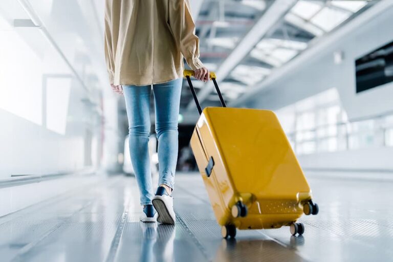 空港の連絡通路で黄色いスーツケースを引いて移動する女性旅行者の後ろ姿