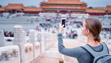 赤い提灯や中国風の装飾が並ぶ深圳の街中で笑顔でスマホを操作する女性旅行者