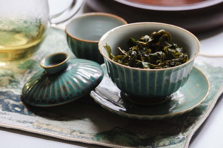 青磁の蓋碗に入った中国茶の茶葉とガラスポットに注がれた黄金色のお茶