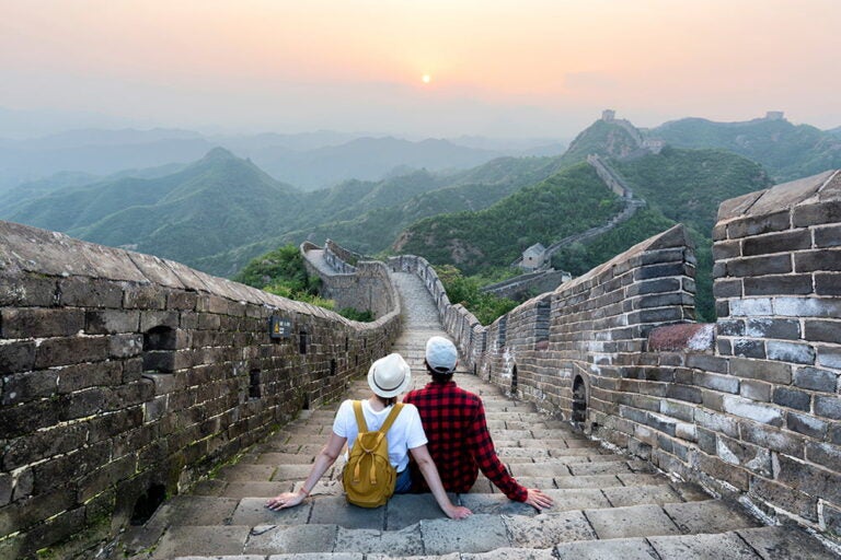 万里の長城の城壁に腰を下ろし、夕暮れの山並みに続く長城の絶景を眺める二人の旅行者
