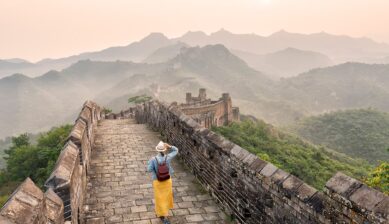 朝もやに霞む山々を背景に、万里の長城の石畳の道を奥へ歩いていく旅行者の後ろ姿