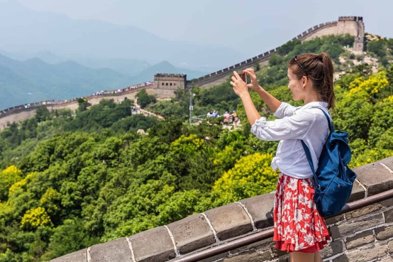 万里の長城の城壁から緑豊かな山並みに続く長城の全景をスマートフォンで撮影する旅行者