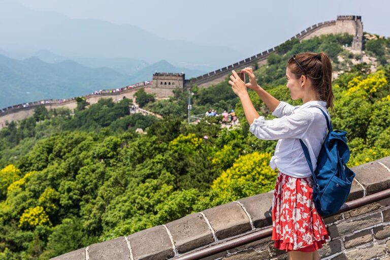  夏の万里の長城で城壁から緑の山々に続く長城をスマートフォンで撮影する旅行者