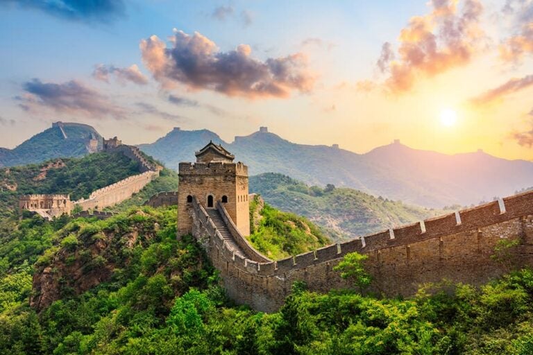 夕陽に照らされた万里の長城の望楼と、緑の山々の稜線に沿ってどこまでも続く城壁の全景
