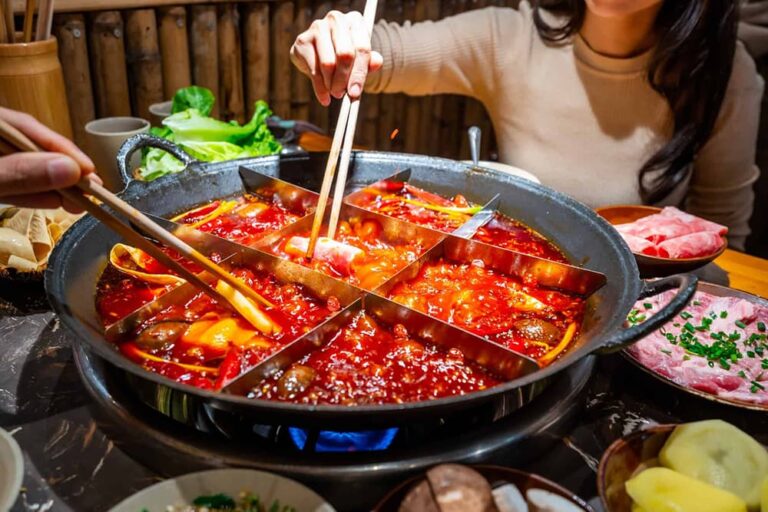 仕切り付きの鍋に真っ赤な麻辣スープが煮立つ中国式火鍋を箸で楽しむ様子