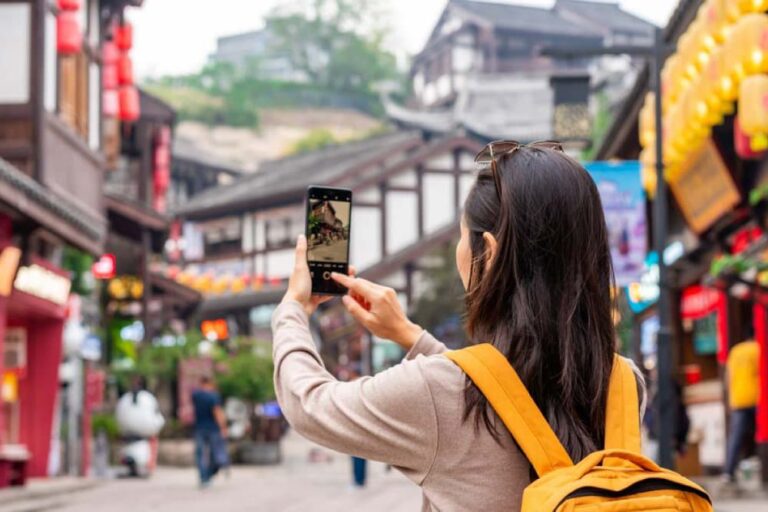  広州の伝統的な街並みでスマートフォンを構えて写真を撮る旅行者の後ろ姿。通り沿いには赤や黄色の提灯が並ぶ