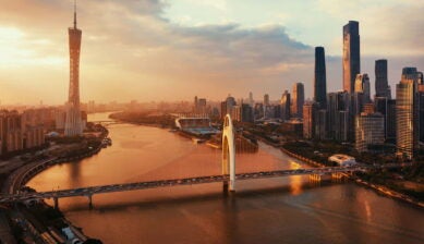 夕暮れの広州市街を空撮で捉えた風景。珠江沿いに広州タワーや高層ビル群が並び、橋を行き交う車の光が都市の活気を伝えている