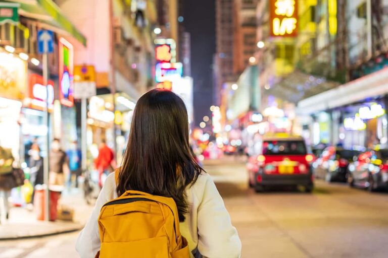 ネオン看板が輝く中国の繁華街を歩く黄色いリュックの女性旅行者の後ろ姿