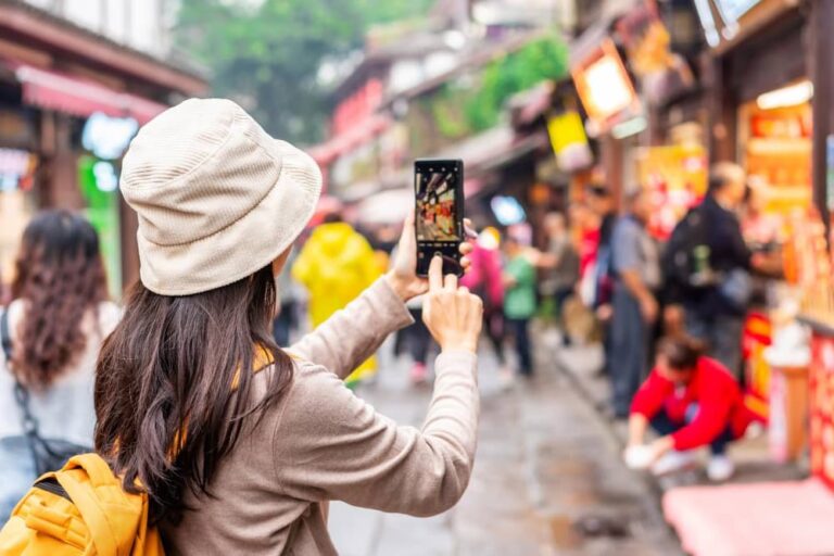 中国の賑やかな商店街でスマートフォンを構えて街並みを撮影する女性旅行者の後ろ姿