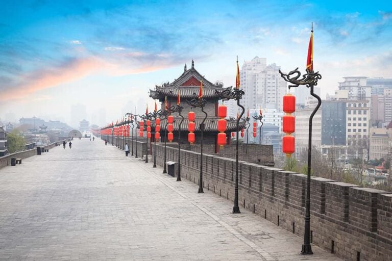 赤い提灯と龍の装飾が並ぶ西安の古城壁の上から望む街並みと夕焼け空
