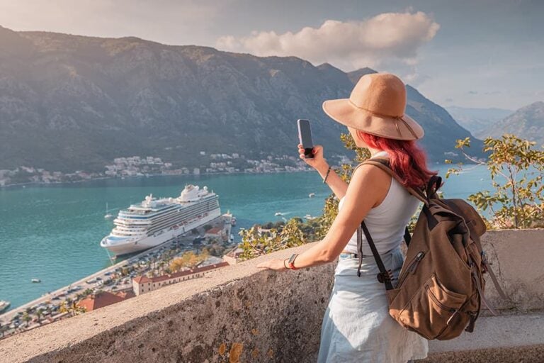 ヨーロッパの湾を見渡す高台でスマートフォンを手に景色を楽しむ女性旅行者