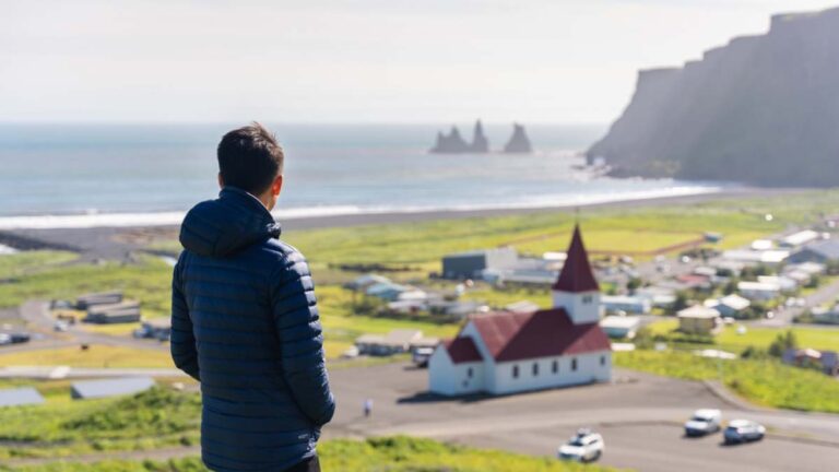 ヨーロッパで最も治安が良いとされるアイスランドのヴィークにて、赤い屋根の教会と美しい海岸線を高台から穏やかに眺める旅行者の様子