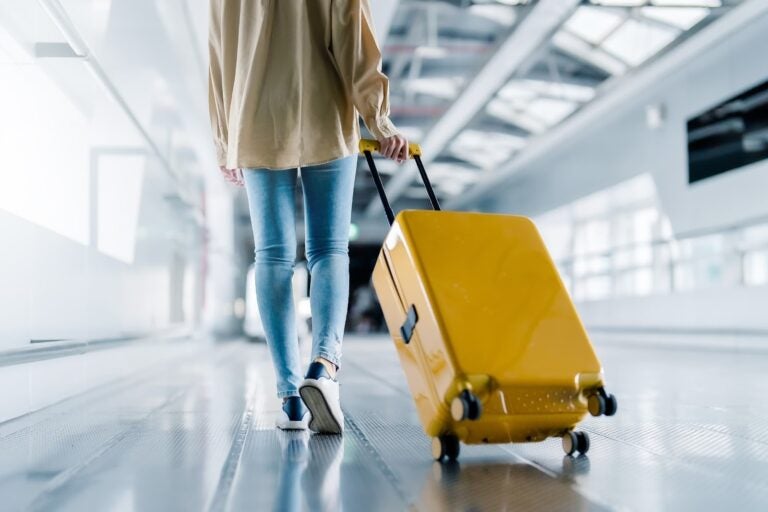 空港の通路で黄色いスーツケースを引いて歩く女性旅行者の後ろ姿