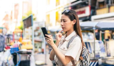 街中でスマートフォンのエラー画面を困った表情で確認する女性のイメージ