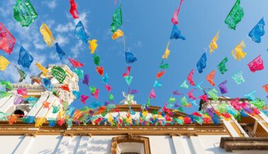 青空に映えるカラフルなパペルピカドが飾られたメキシコの白い教会