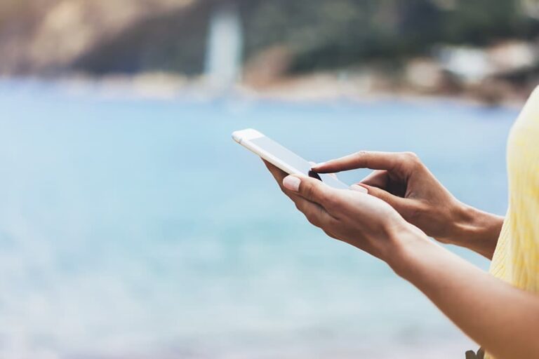  海辺でスマートフォンを使い旅行中の情報確認をする様子