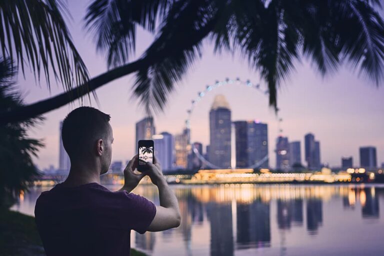 夜景のシンガポール都市景観をスマートフォンで撮影する男性旅行者のイメージ