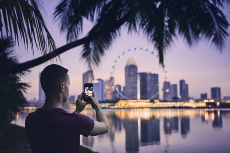 夜景のシンガポール都市景観をスマートフォンで撮影する男性旅行者のイメージ