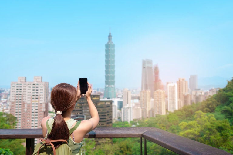 台北101を背景にスマートフォンで撮影する女性旅行者のイメージ