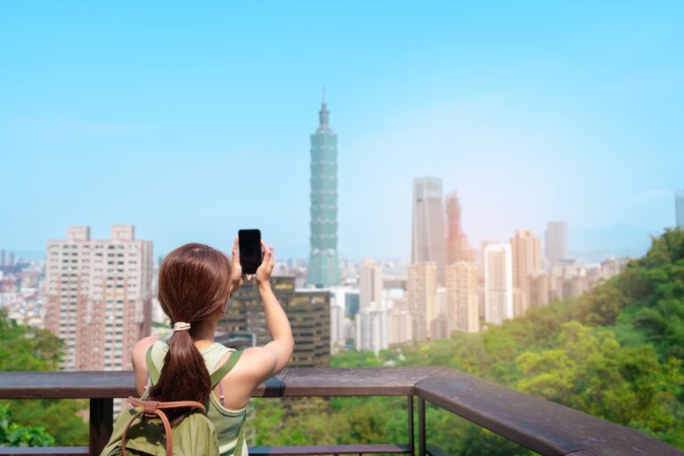 台北101を背景にスマートフォンで撮影する女性旅行者のイメージ