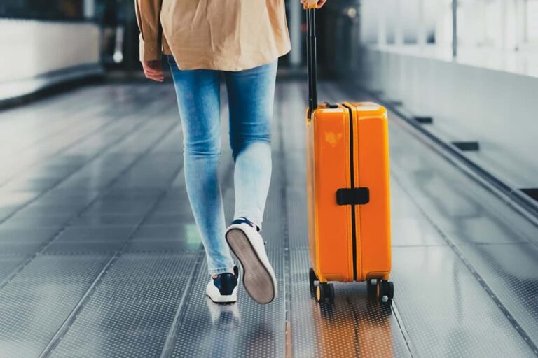  空港の通路で黄色いスーツケースを引いて歩く女性旅行者の後ろ姿