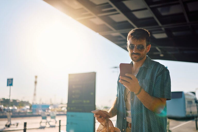 海外WiFiを使いながら空港でスマートフォンを操作する男性旅行者のイメージ