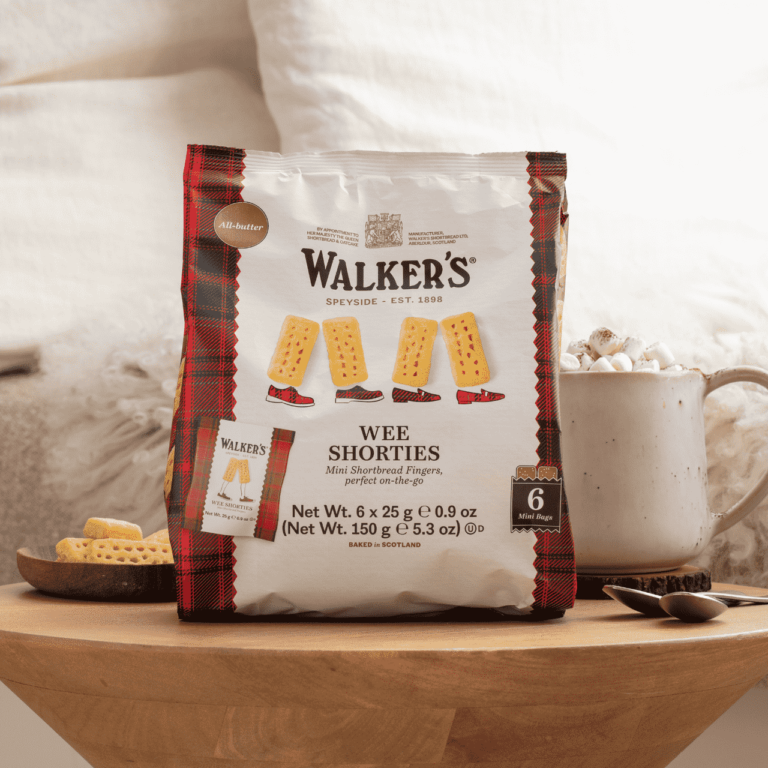 イギリス土産の定番、ウォーカーズ(Walker's)の個包装ミニショートブレッド「WEE SHORTIES」。赤いタータンチェックが目印のパッケージと、温かい飲み物が置かれたテーブルの様子。