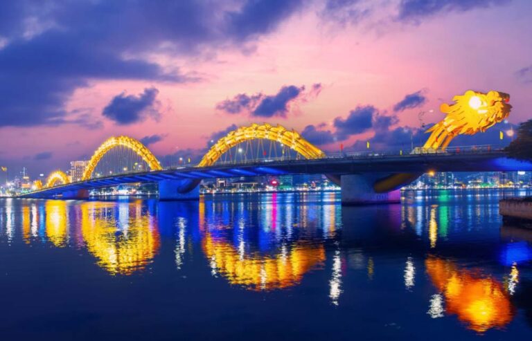 夕暮れにライトアップされたダナンのドラゴンブリッジと川面の反射