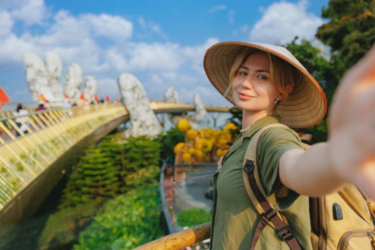 ダナンのゴールデンブリッジでノンラーをかぶり笑顔で自撮りする女性観光客