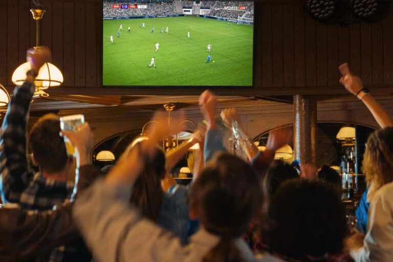 バーでサッカーワールドカップ2026の日本代表戦をテレビ観戦する盛り上がるサポーターのイメージ