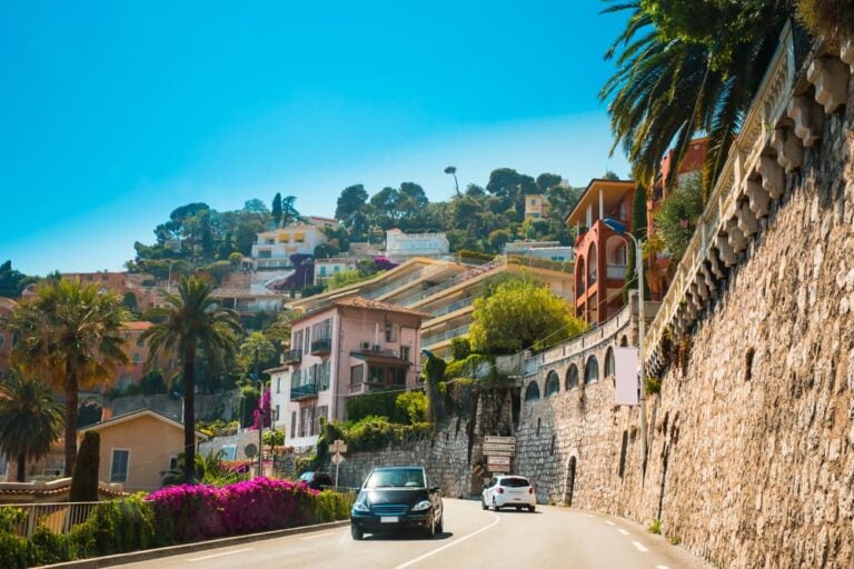 ヤシの木と地中海沿いの街並みが広がる南フランス・コートダジュールの海岸沿いの道路を走る車