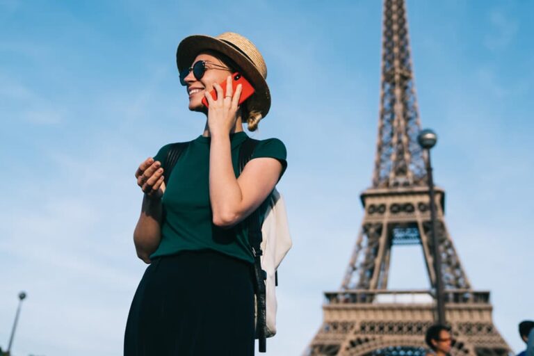 エッフェル塔の前でスマートフォンを使うパリ旅行中の女性