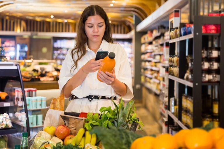 ドイツのスーパーマーケットでスマホ片手に商品を選ぶ女性の買い物風景
