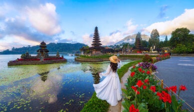 晴天のバリ島ウルン・ダヌ・ブラタン寺院を訪れる、白いワンピース姿の女性旅行者