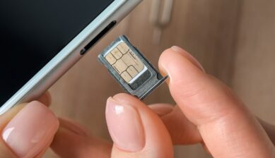 iPhoneから取り出したSIMトレイとnanoSIMカードを指でつまんでいるクローズアップ